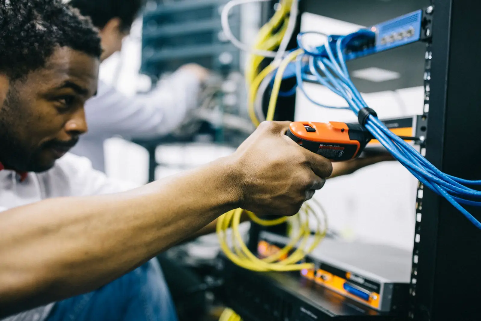 Engineer terminating network cables at a rack (illustrative stock photograph)