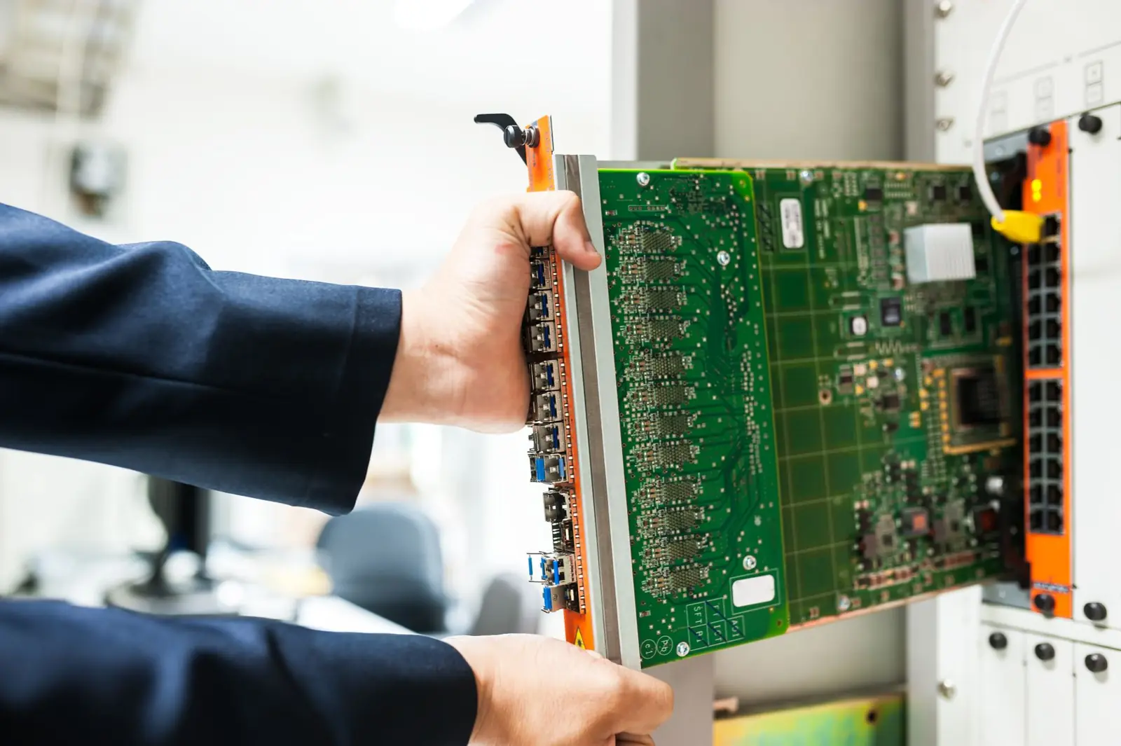 Technician fitting a circuit card into a rack-mounted chassis (illustrative stock photograph)